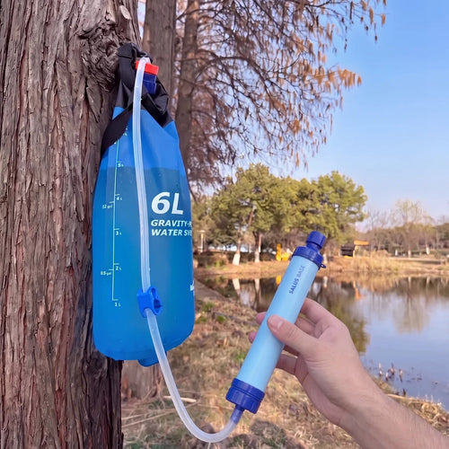 RESERVE-X1 6L gravity water bag hanging from a tree, hose connected to the AQUA-X1 filter straw